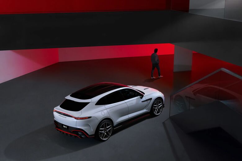 Witte Aston Martin DBX S in een rood verlichte ruimte met een figuur op de achtergrond