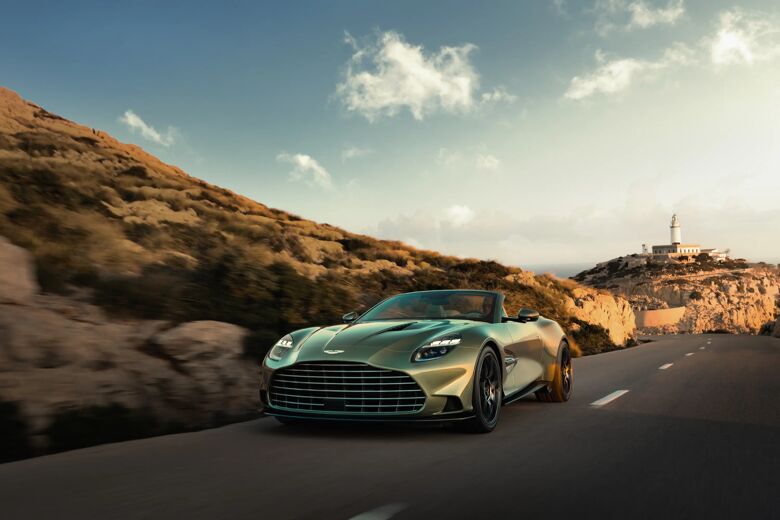 Groene Aston Martin Vanquish Volante met open dak rijdt over een kustweg, met vuurtoren op de achtergrond