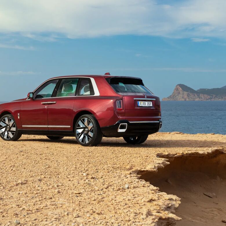 Rolls-Royce Cullinan in Scala Red geparkeerd op de rotsen aan de kust