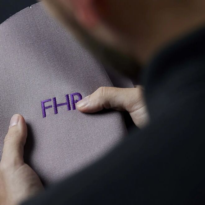 Persoon houdt een lila stofstaal met FHR-monogram tegen zijn schouder