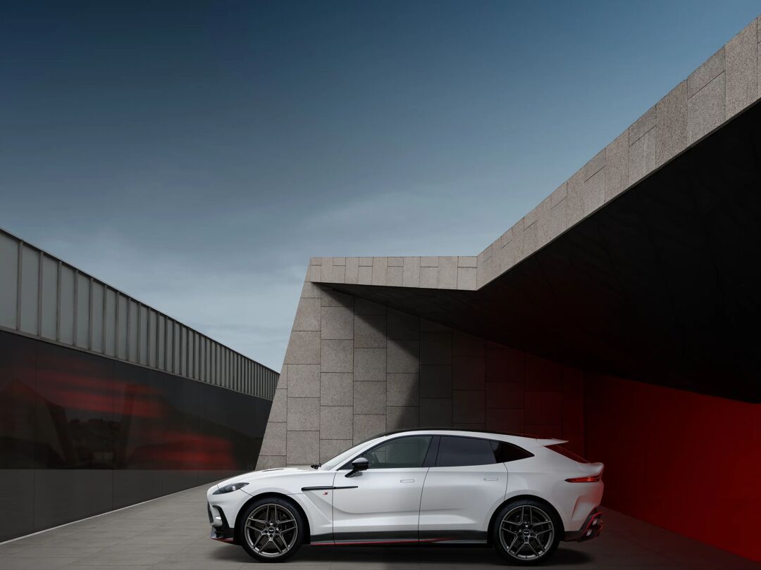 Witte Aston Martin DBX S in zijaanzicht bij betonnen architectuur in de schemering