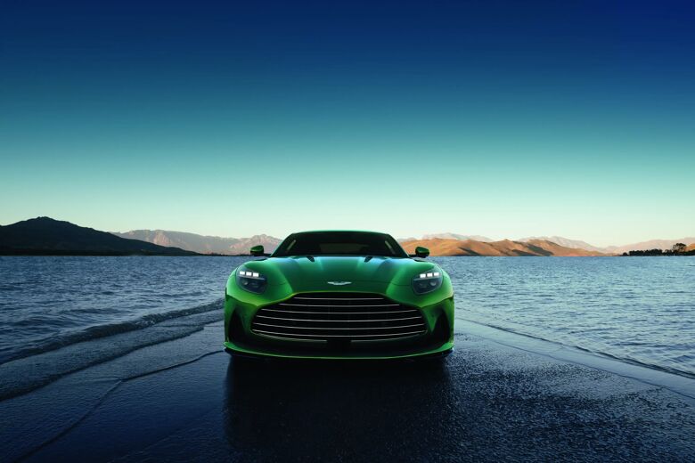 Groene Aston Martin DB12 recht van voren bij water in de schemering, met spiegeling