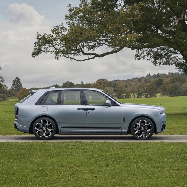 Rolls-Royce Cullinan Black Badge in lichtblauwe kleur, zijaanzicht op landgoed met grote boom