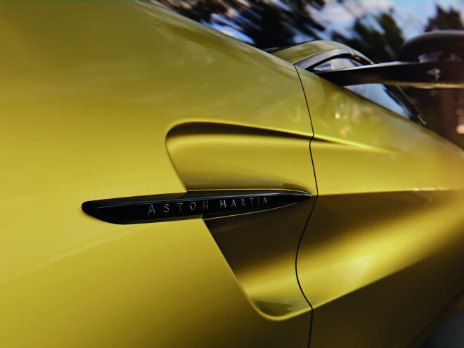 Detail van de zijflank van de gele Aston Martin Vantage met Aston Martin badge in de luchtinlaat